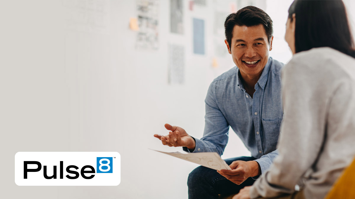 Man holding a paper smiling while talking to a woman with Pulse8 logo