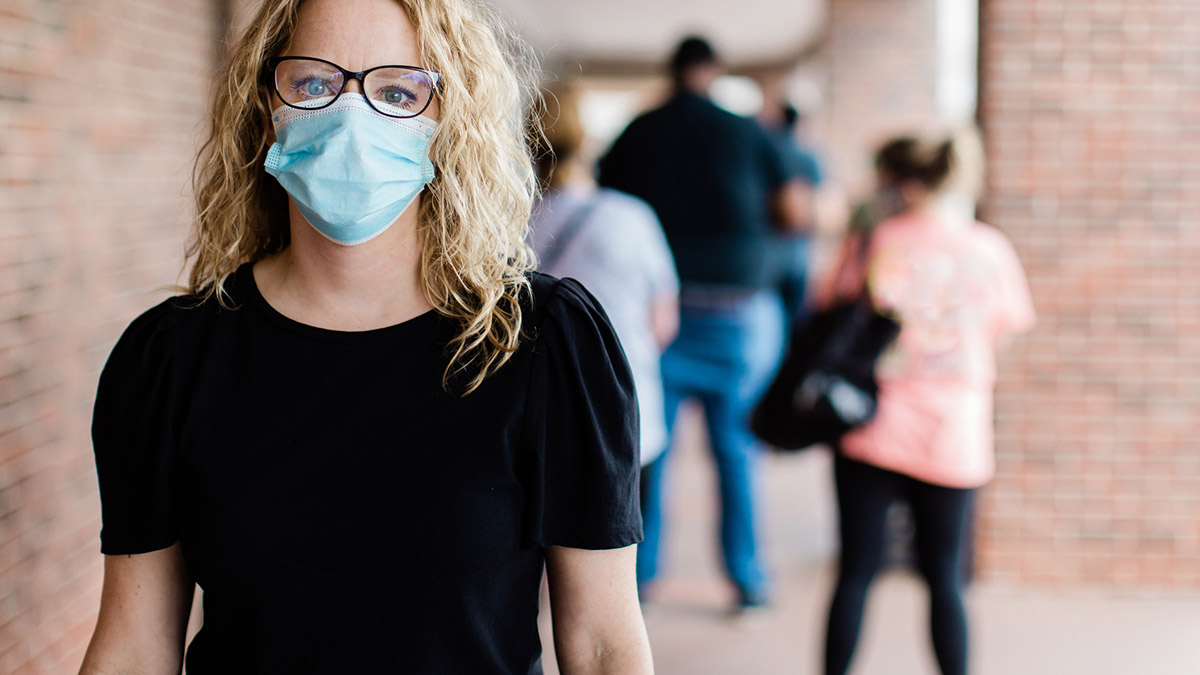 A woman wearing a surgical mask with people in the background