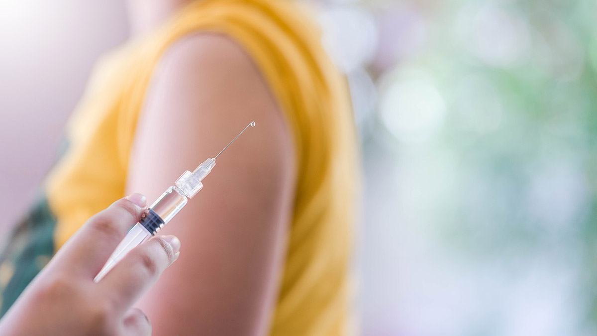 Close-up of a person holding a syringe with someone's arm in the background