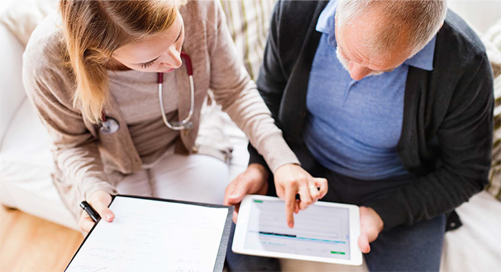 Young doctor sitting down with older patient pointing to health records on a tablet